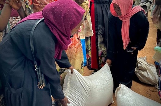 A couple of women with headscarves lifting a bag of food.