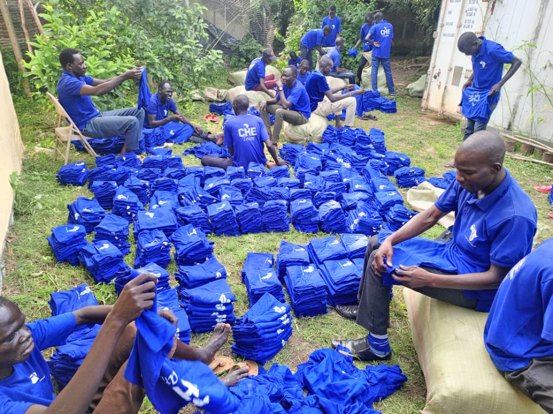 A group of people sitting on the grass with piles of blue shirts